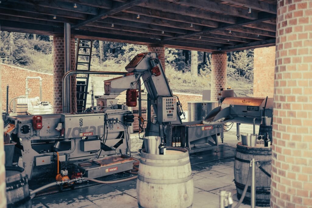 Machinery setup in a vineyard's outdoor shelter with barrels, used in wine production.